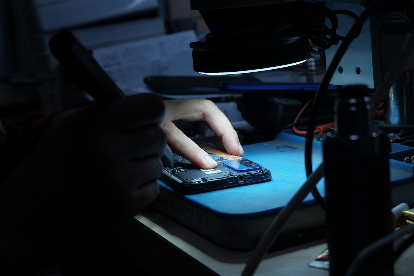 Mains réparant un smartphone sur un tapis bleu avec des outils.