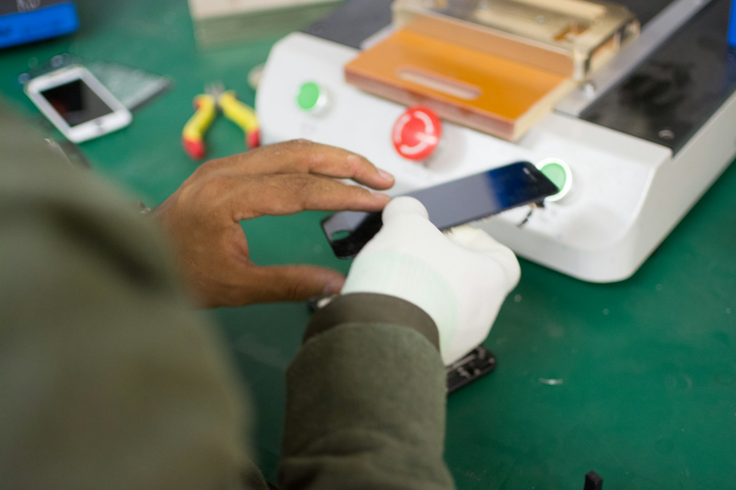 Technicien réparant un smartphone sur un établi vert.
