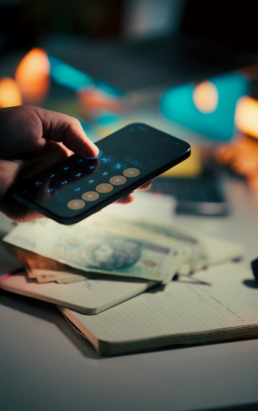 Main utilisant une calculatrice sur smartphone avec de l'argent et un carnet.